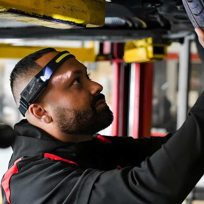 Person using a headlamp under a vehicle in an automotive setting